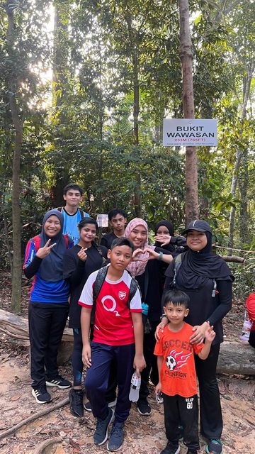 Colleagues and family at the Bukit Wawasan summit marker, the trail and forest behind them.