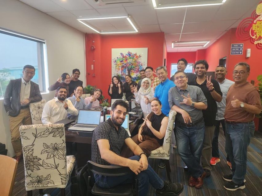 The office team gathered around a desk for a group photograph, Chinese New Year decorations on the wall behind them.