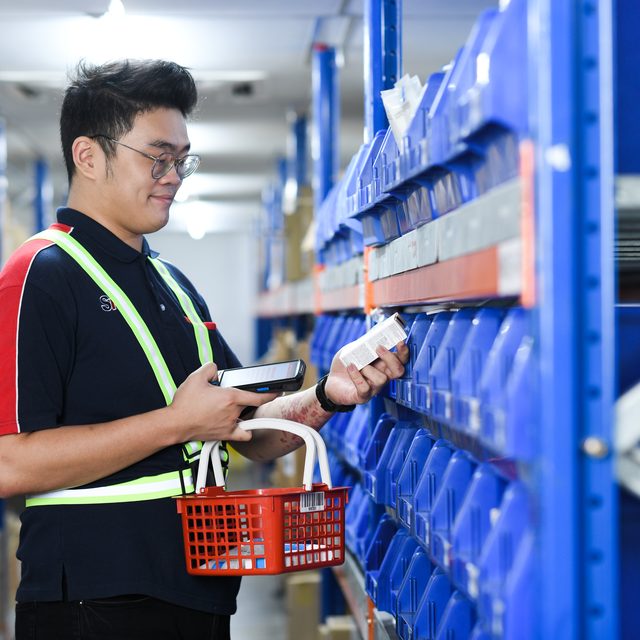 An operator scanning an item at a pick face, a handheld in one hand and a picking basket on his arm.