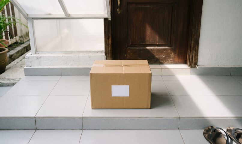 A parcel left on a tiled doorstep in front of a timber door.